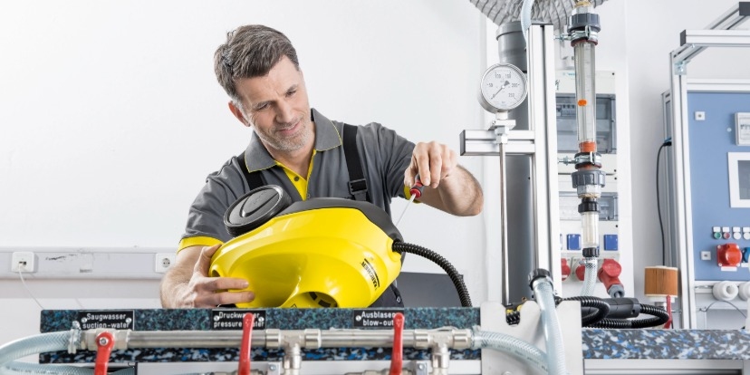 Ein Techniker führt im Rahmen des Kärcher Service eine professionelle Reparatur an einem gelben Kärcher Reinigungsgerät in einer spezialisierten Werkstatt durch, um eine optimale Funktion zu gewährleisten