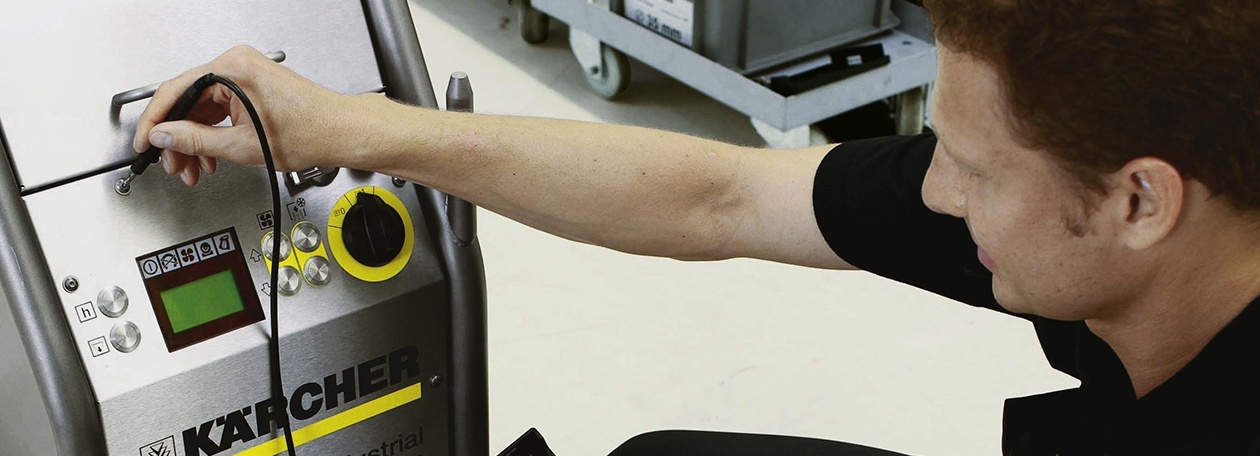 Präziser Werkskundendienst der Alfred Kärcher GmbH: Technische Diagnose am Gerät Ein Servicetechniker der Alfred Kärcher GmbH führt eine technische Prüfung an einer Industrie-Reinigungsmaschine aus Edelstahl durch. Er hält eine Messspitze an das Gehäuse oberhalb des Bedienfelds, auf dem das Kärcher-Logo, ein digitales Display und mehr