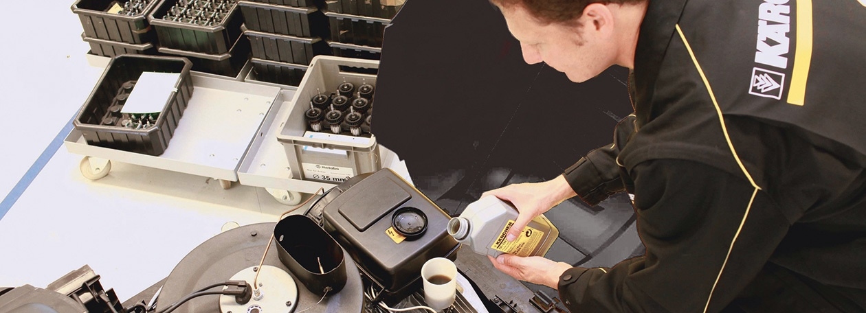 Ein Techniker des Unternehmens Kärcher befüllt eine professionelle Reinigungsmaschine in einer Werkstatt mit originalen Betriebsstoffen, um eine fachgerechte Wartung durchzuführen.