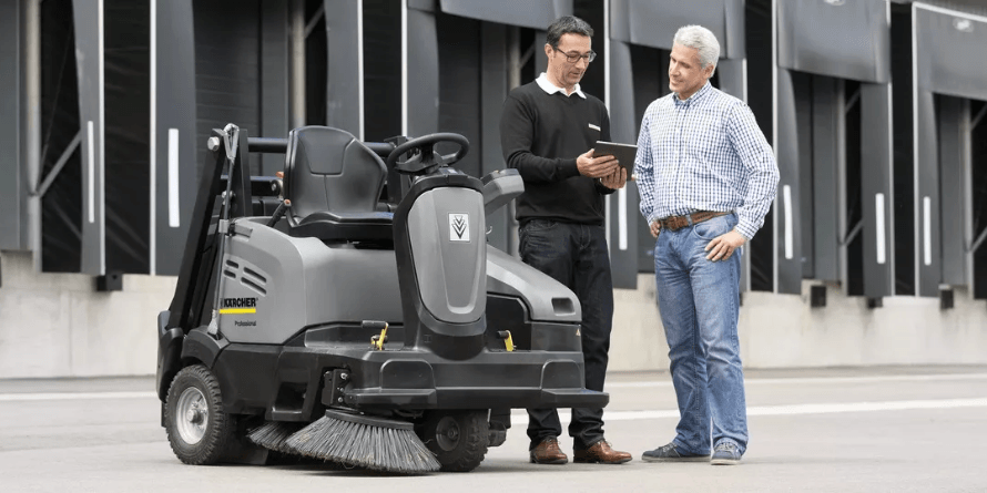 Ein Kärcher Servicepartner im Beratungsgespräch mit einem Kunden neben einer professionellen Kärcher Aufsitz-Kehrmaschine.