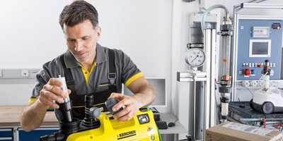 Professioneller Kärcher Reparaturservice und Wartung in der Fachwerkstatt Ein Kärcher Servicetechniker in grau-gelber Arbeitskleidung arbeitet konzentriert an einem gelben Kärcher Gerät in einer Werkstattumgebung.
