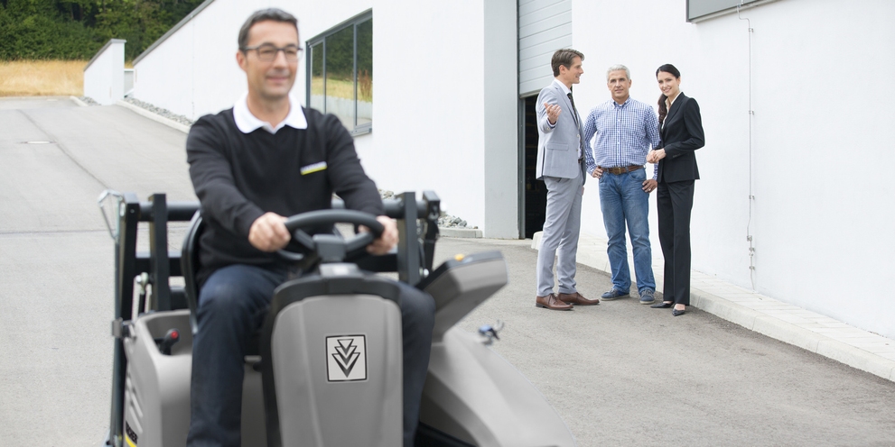 Kärcher Produktvorführung: Fachberatung und Maschinendemonstration vor Ort Ein Mitarbeiter bedient im Vordergrund eine Kärcher Professional Aufsitz-Reinigungsmaschine