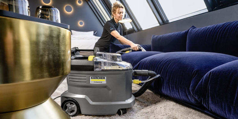 Eine Frau reinigt ein dunkelblaues Sofa in einem modernen Raum mit einem Kärcher Professional Waschsauger.