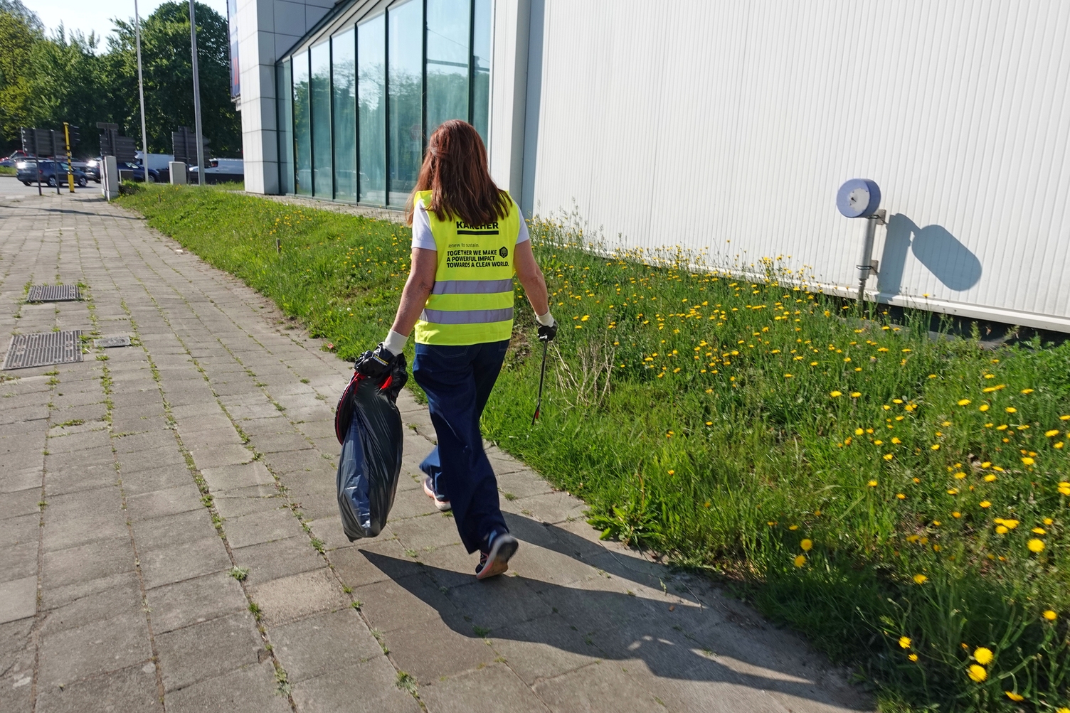 Une femme en gilet jaune Kärcher marche avec un sac poubelle sur le trottoir lors d'un nettoyage