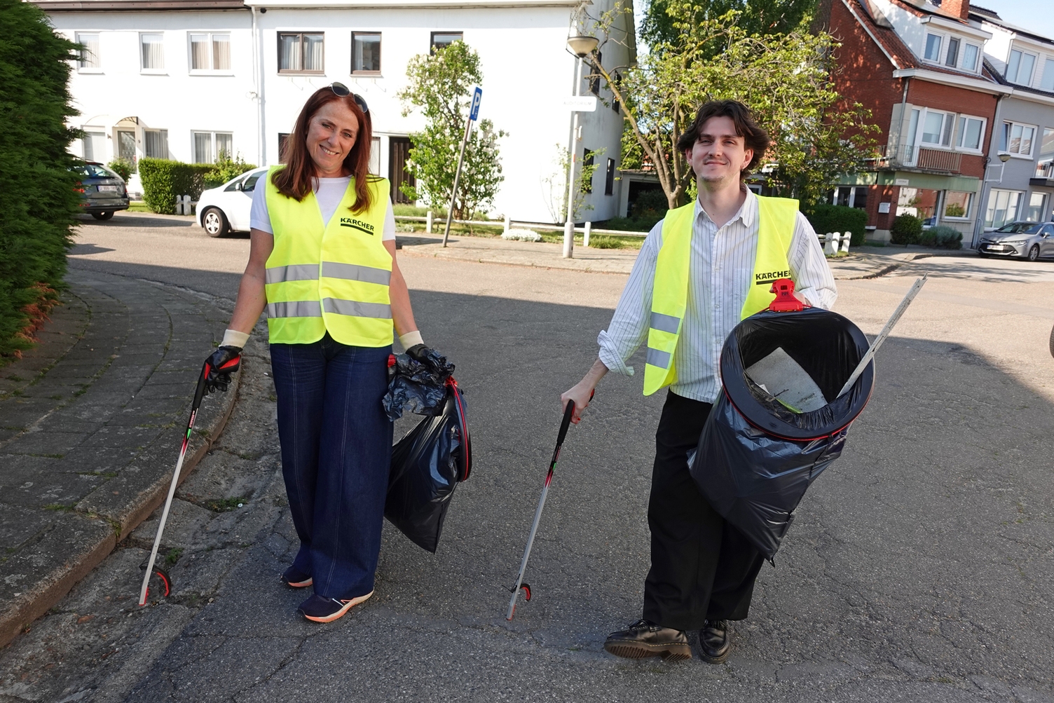 Deux employés Kärcher souriants en gilets jaunes ramassent les déchets avec des pinces dans la rue
