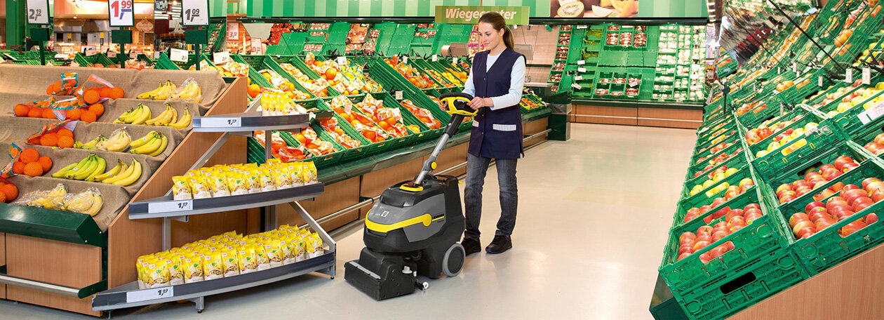 Vrouw bedient een handgeleide schrobmachine in een groente- en fruitwinkel Vrouw bedient een handgeleide schrobmachine in een groente- en fruitwinkel