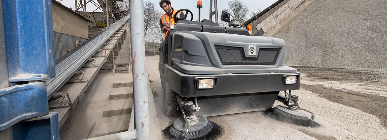 Bediener van een industrële zitveegmachine die een industrieterrein veegt