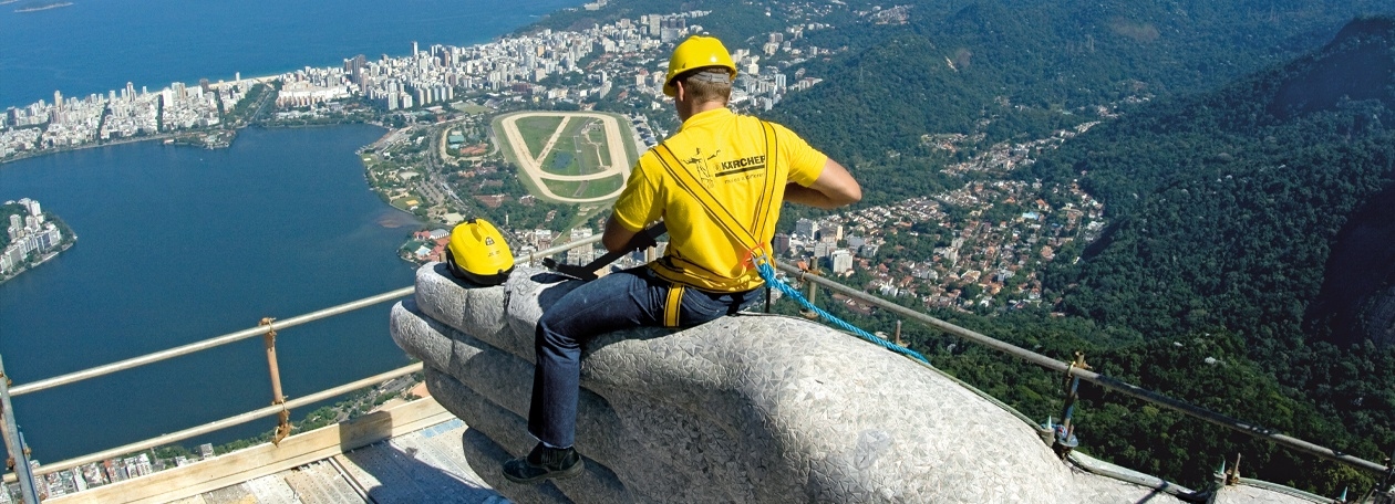 Fijnzandstraalreiniging van de zeepstenen mozaïekbekleding op de Corcovado-heuvel Een Kärcher-technicus zit op de arm van het Christusbeeld in Rio de Janeiro tijdens de reinigingswerkzaamheden.