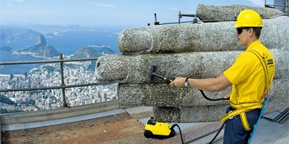 Nauwkeurige fijnzandstraalmethode op de gevoelige zeepstenen mozaïektegels Technicus reinigt de rechterhand van het Christusbeeld met de stad Rio de Janeiro op de achtergrond.