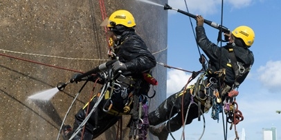 Het krachtig verwijderen van de vuilkorst met 200 bar waterdruk op grote hoogte Twee industriële klimmers spuiten met warm water onder hoge druk het beton van de Euromast schoon.