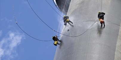 Toepassing van 200 bar warm water onder hoge druk om de hardnekkige vuilkorst te verwijderen Drie klimmers hangen aan touwen aan de betonwand van de Euromast tijdens de reinigingswerkzaamheden.