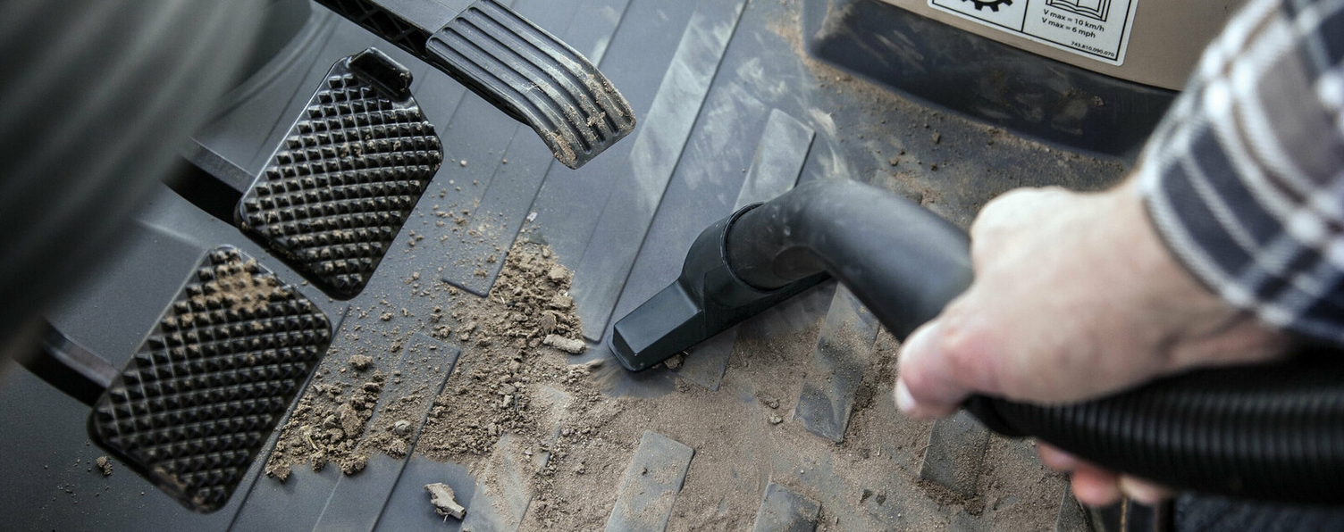 Een hand gebruikt een Kärcher stofzuiger om de binnenkant van een cabine te reinigen