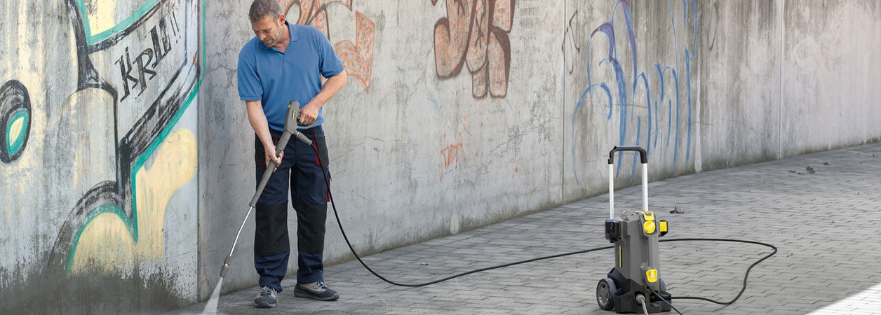 graffiti hogedrukreiniger Man gebruikt hogedrukreiniger om tegels schoon te maken naast een muur vol graffiti