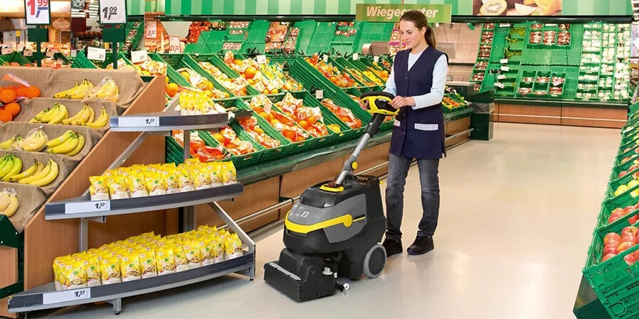 Vrouw gebruikt handgeleide schrobzuigmachine in supermarkt
