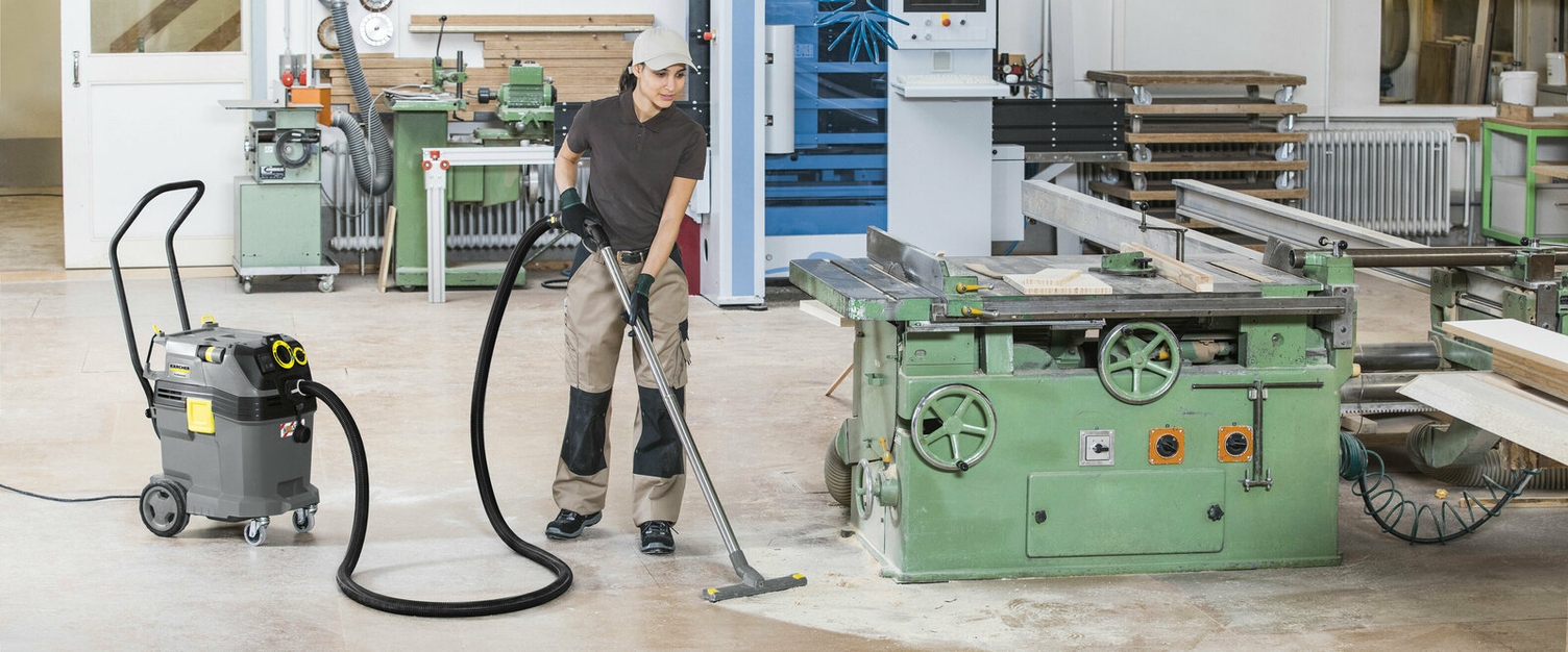 Houtstof afzuigen een persoon reinigt de vloer van een werkplaats met een Kärcher stofzuiger