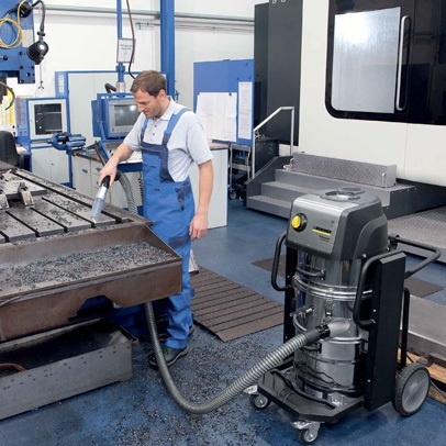 Een medewerker reinigt een industriële machine met een krachtige Kärcher industriële stofzuiger