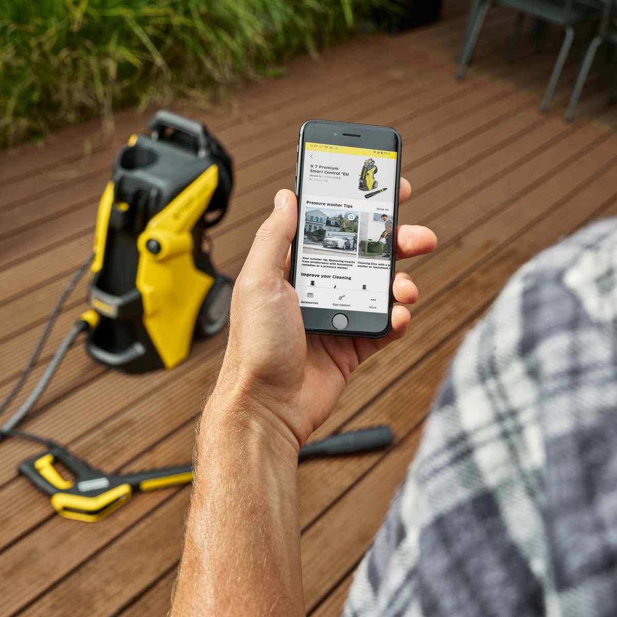 Gebruiker raadpleegt de Kärcher Home & Garden app op een smartphone bij een Kärcher hogedrukreiniger op een houten terras