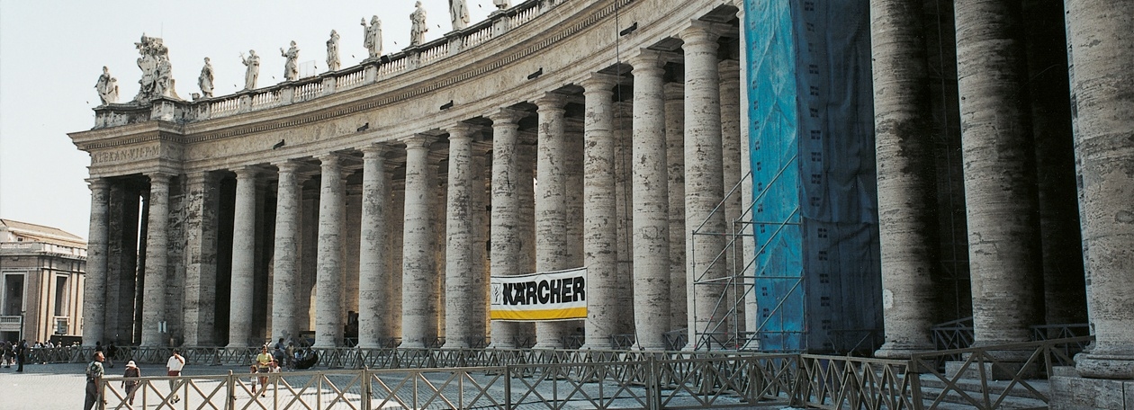 Gereinigde travertijnzuilen van de Bernini-colonnades op het Sint-Pietersplein met een Kärcher-spandoek.
