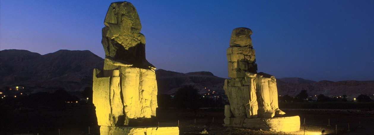 De 3300 jaar oude kwartsieten Memnonkolossen voor de voormalige dodentempel van Amenophis III De twee verlichte Memnonkolossen in het avondlicht in westelijk Thebe, Egypte.