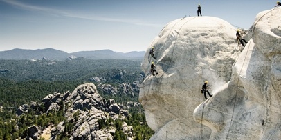 Overzichtsfoto van het landschap rond Mount Rushmore met klimmers op de presidentenhoofden.