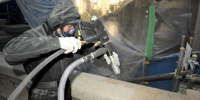 Voorzichtig verwijderen van de zwarte afzetlaag met calciumcarbonaat en aluminiumsilicaat Een technicus in beschermende kleding verwijdert roet en vuil van de brug met een straalpistool.