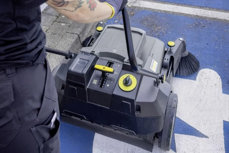 Persoon gebruikt veegmachine om parkeerplaatsen schoon te maken