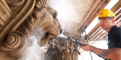 Nauwkeurige reiniging van de historische leeuwensculptuur Een restaurateur reinigt een gedetailleerd zandstenen leeuwenkop-ornament op de gevel van het theater in Praag.