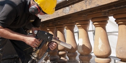 Nauwkeurige reiniging van de balustrade-elementen om zwarte aanslag en oude lagen te verwijderen Een specialist reinigt de stenen balusters van de theaterbalustrade met een Kärcher-straalpistool.