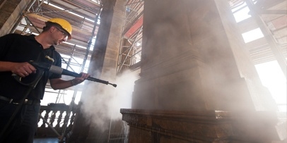 Verwijdering van hardnekkige vuilafzetting op de grote steenelementen van het theater Een restaurateur reinigt een grote stenen zuil met een Kärcher-hogedrukreiniger.