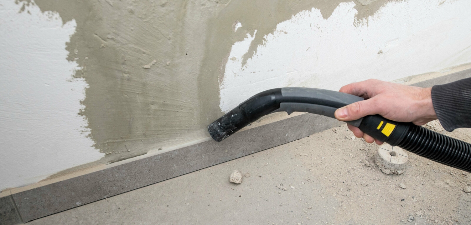 Een hand gebruikt een Kärcher stofzuiger om resten van een bewerkte muur te verwijderen
