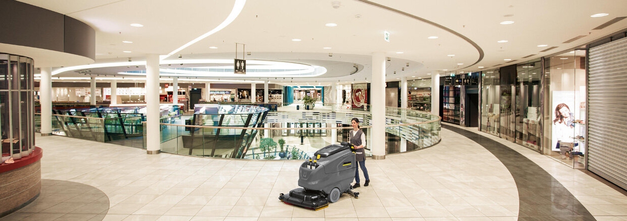 Vrouw gebruikt schrob-/zuigmachine om schoon te maken in een winkelcentrum