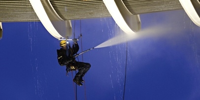 Horizontale bereikbaarheid van het overhangende platform als speciale uitdaging op hoogte Een industriële klimmer met hoofdlamp reinigt de onderzijde van het drie verdiepingen tellende torenplatform.