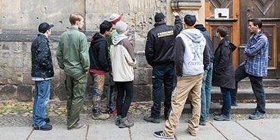 Een Kärcher-specialist geeft een groep jongeren uitleg over de verontreiniging en structuur van een historische gevel.