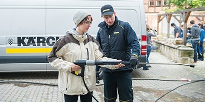 Een Kärcher-expert begeleidt een studente bij het vasthouden en bedienen van een professionele hogedruklans.
