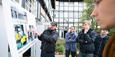 Een instructeur legt aan jongeren de werkwijze van historische restauraties uit aan de hand van voorbeeldfoto's.