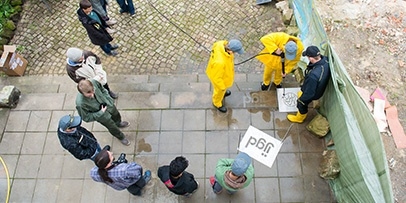 Bovenaanzicht van de groep jongeren in gele beschermkleding die instructies krijgen op een stenen trap.