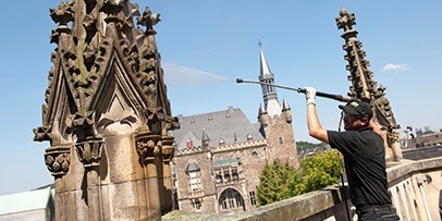 Een industriële klimmer van Kärcher reinigt met een warmwater-hogedrukreiniger gotische ornamenten op het dak van een kathedraal.