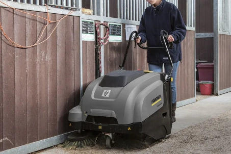 Persoon gebruikt veegmachine om stal schoon te maken