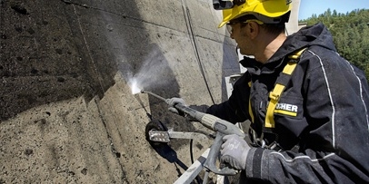 Het creëren van de details van de forellen door het gericht verwijderen van de 30 jaar oude vuillaag Close-up van een Kärcher-technicus die algen en vuil van het beton spuit met een HD 13/18-4 S koudwater-hogedrukreiniger.