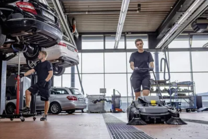 Persoon gebruikt veegmachine om autowerkplaats schoon te maken