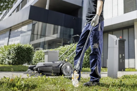 Persoon maakt tuin van appartementsgebouw schoon met veegmachine