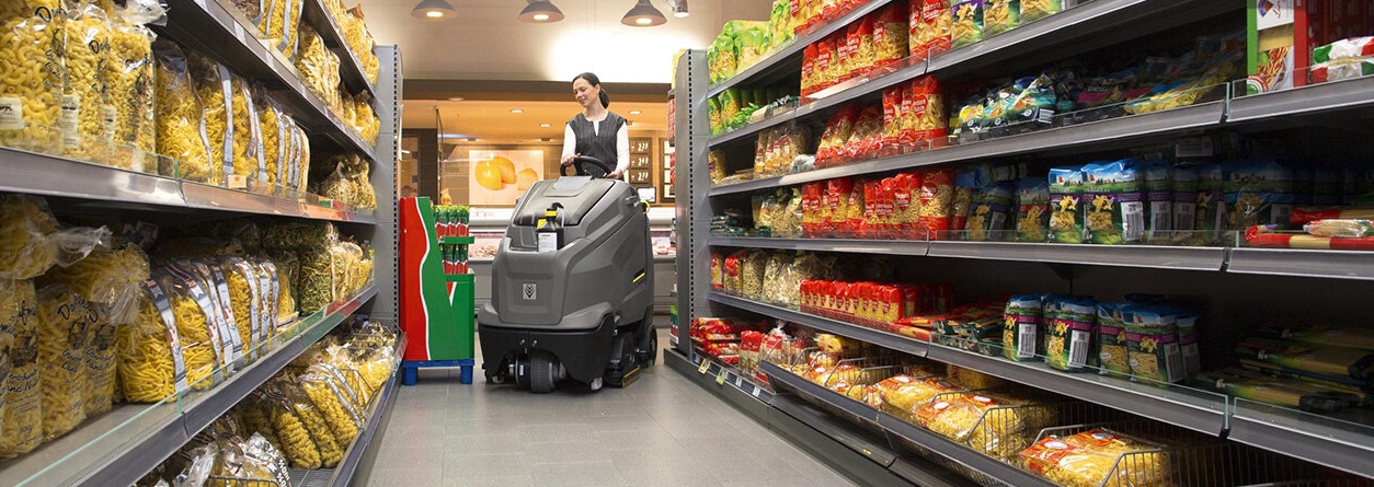 Vrouw gebruikt walk-behind schrob-/zuigmachine om de supermarkt schoon te maken
