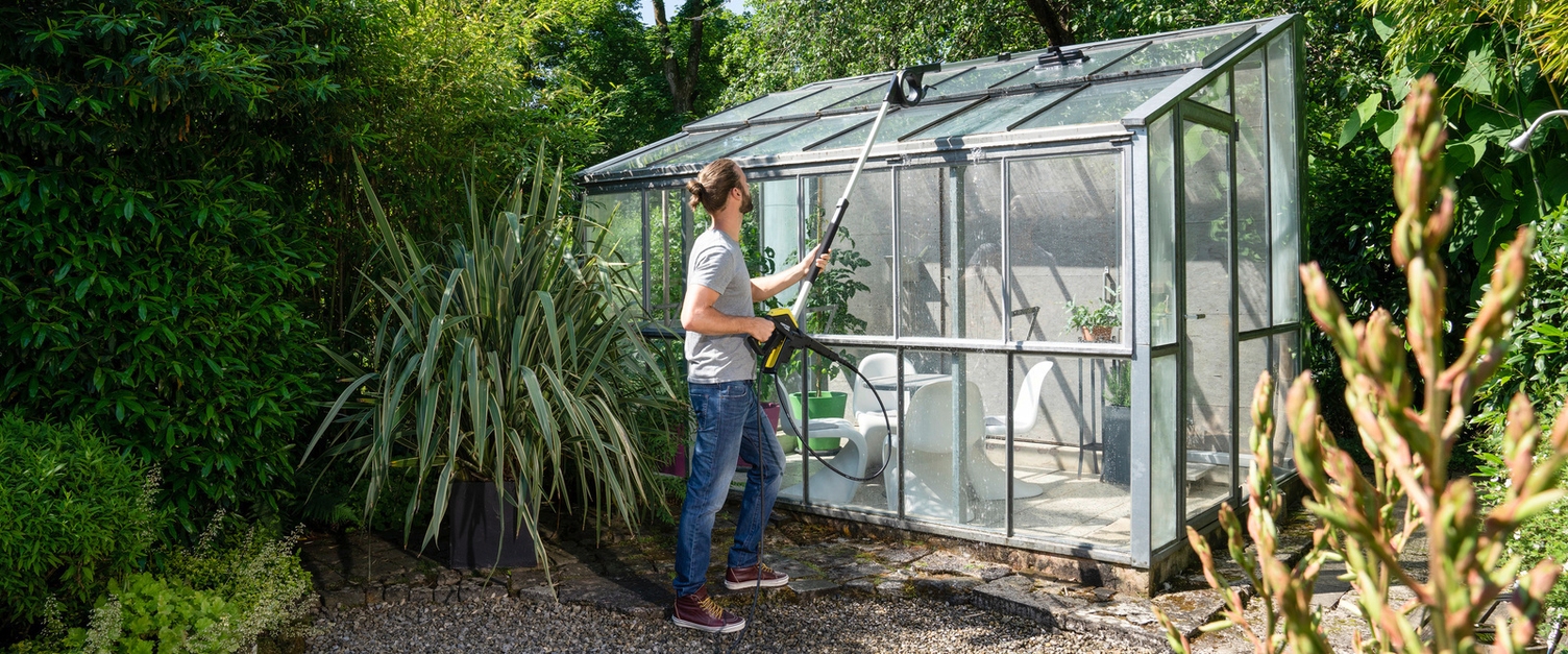 De serre of tuinkas schoonmaken Man reinigt zijn serre met een telescopische spuitlans van Kärcher