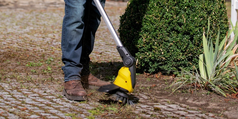 Een persoon verwijdert onkruid tussen de straatstenen met de Kärcher draadloze onkruidverwijderaar