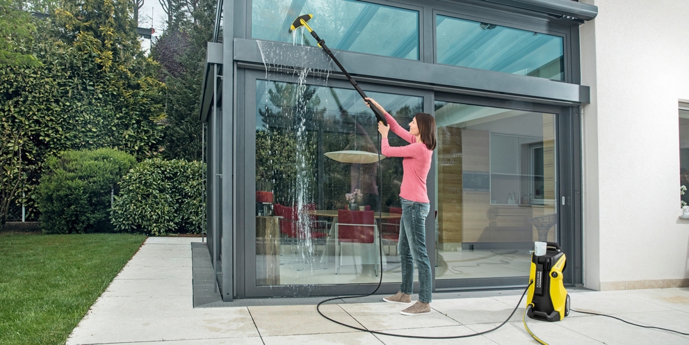 De serre schoonmaken met een hogedrukreiniger en een wasborstel Vrouw reinigt een serre met een Kärcher hogedrukreiniger