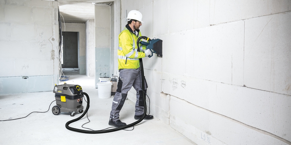 een man in bouwkleding reinigt een muur in aanbouw met een veiligheidsstofzuiger