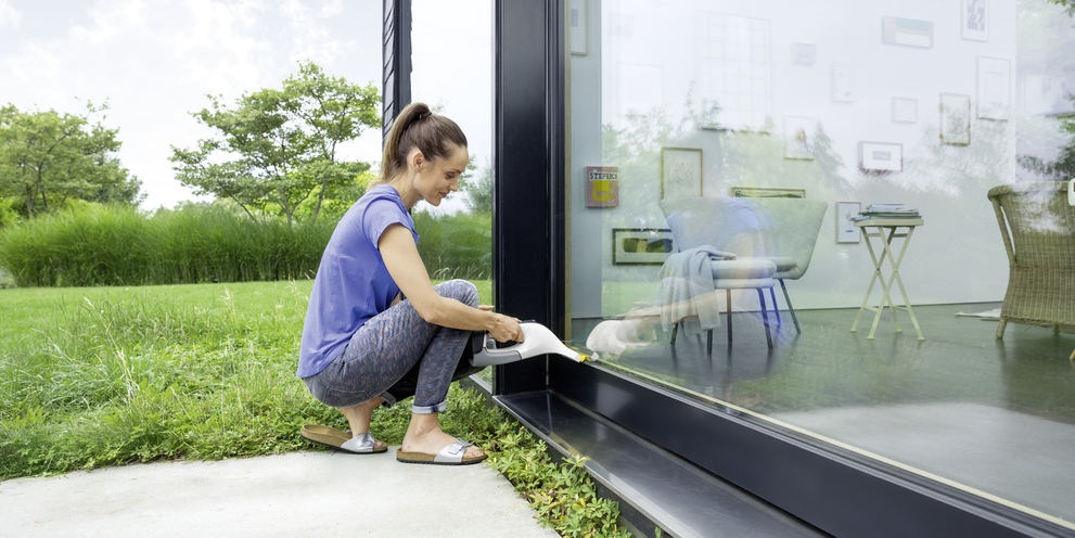 De serre schoonmaken met een vibrerende ramenwisser en een Window Vac Vrouw reinigt haar serre met een vibrerende ramenwisser van Kärcher
