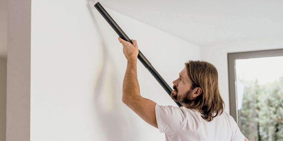 Man zuigt het plafond van zijn huis met behulp van een verlengstuk