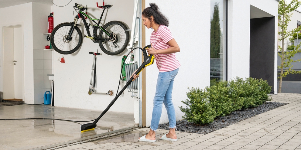 De garagevloer reinigen met water Vrouw reinigt haar garagevloer met een Kärcher wasborstel