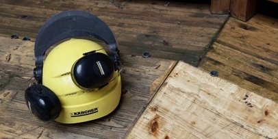 Een gele Kärcher-veiligheidshelm met gehoorbescherming en visier rust op de houten vloer.